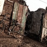 A bike leans against a rusted, weary wall.